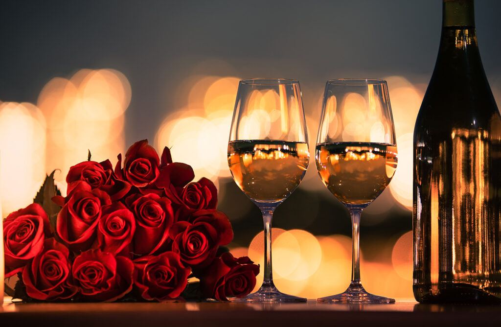 Romantic dinner date night with roses and wine on the table and city lights in the background.