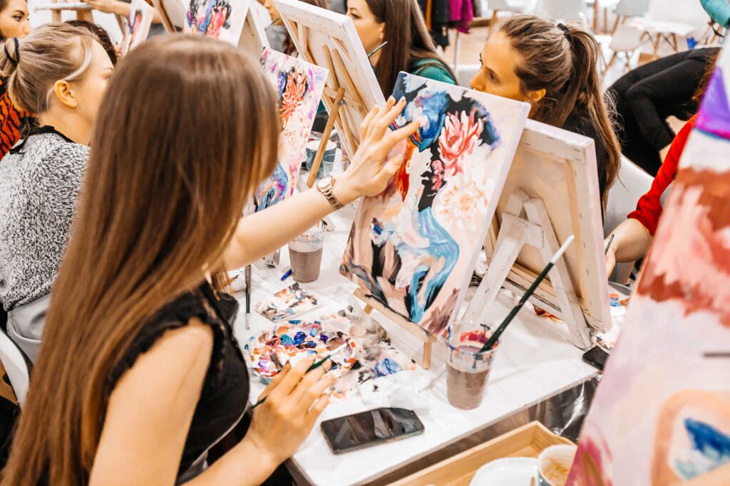 Young women paint with brushes on easels in guided art class