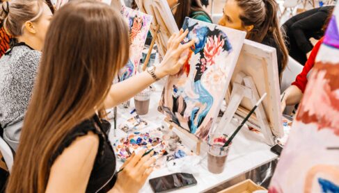 Young women paint with brushes on easels in guided art class